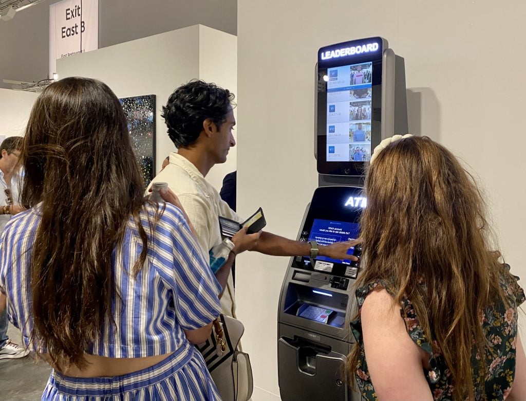 Sameer Khosla add his bank account balance to MSCHF's <em>ATM Leaderboard</em> (2022) at Perrotin's booth at Art Basel Miami Beach. Photo by Sarah Cascone. 