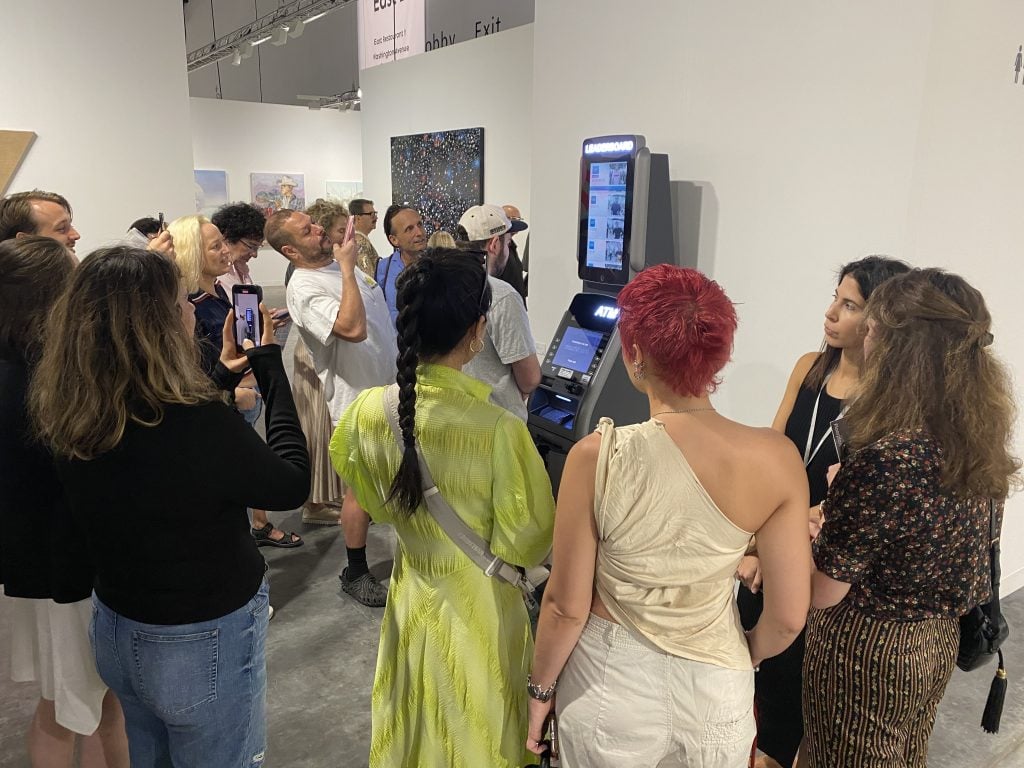 MSCHF's Dan Greenberg adds his bank account balance to the collective's <em>ATM Leaderboard</em> (2022) at Perrotin's booth at Art Basel Miami Beach. Photo by Sarah Cascone. 