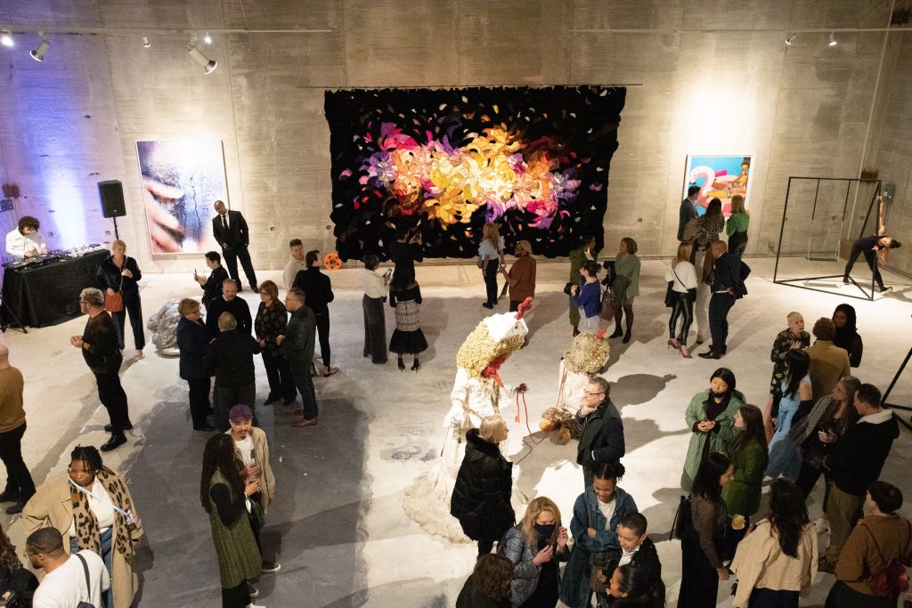 A scene from the opening of "Skin in the Game" in Chicago, with sculptural works by Lynda Benglis and Brendan Fernandes (the latter activated with a performance), paintings by Derrick Adams and Marilyn Minter, an Agustina Woodgate wall tapestry, and a DJ. Photo: Kim Kovacik.