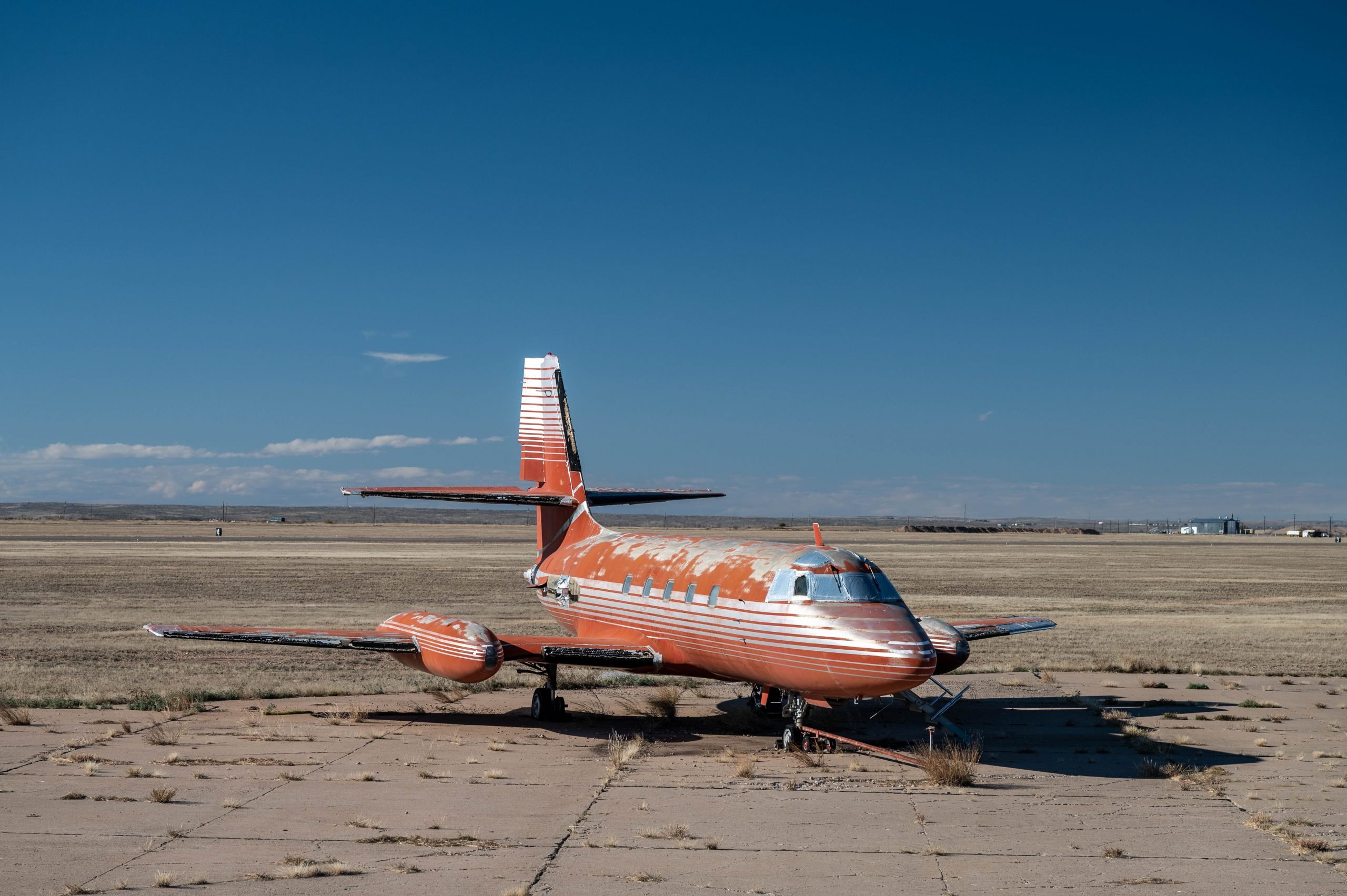 A beat up looking red and silver jet that once belonged to Elvis on a rundown looking tarmac in front of a blue sky.