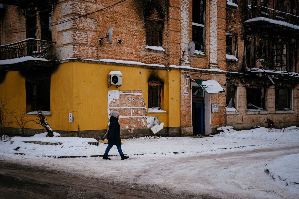 A woman walks near a cut off of the wall of a damaged building from where a group people tried to steal a work of the famous British artist Banksy in the town of Gostomel, near Kyiv, on December 3, 2022, amid the Russian invasion of Ukraine. Photo by Dimitar Dilkoff/AFP via Getty Images.