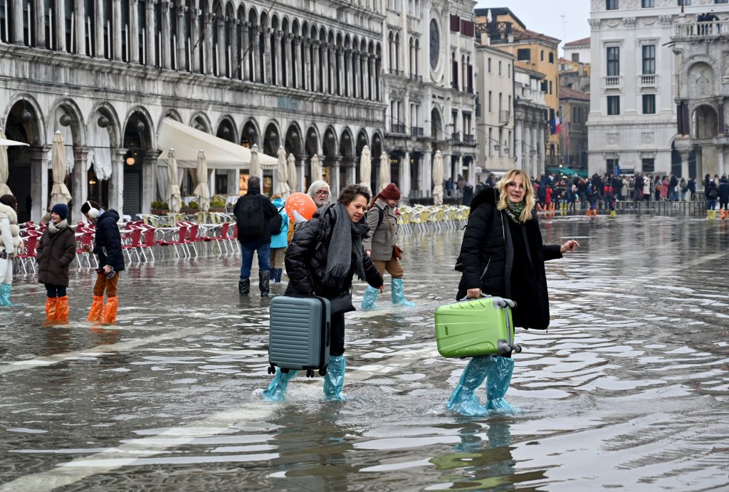Tourists in St. Mark's Square traverse the floodwaters of an Acqua Alta event on December 10, 2022. The high tide was too low to operate the MOSE Experimental Electromechanical Module that protects the city of Venice from floods. Photo by Andrea Pattaro for AFP via Getty Images. 
