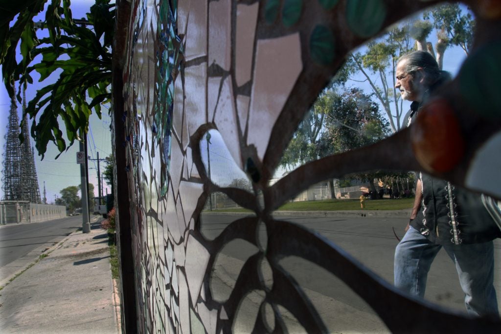 ศิลปิน Augustin Aguirre เดินไปด้านหน้ากำแพงกระเบื้องที่เขาสร้างขึ้นซึ่งเป็นส่วนหนึ่งของการปรับปรุงโครงการ Watts House Project ตรงข้าม Watts Towers  (ภาพ: Bob Chamberlin / Los Angeles Times ผ่าน Getty Images)