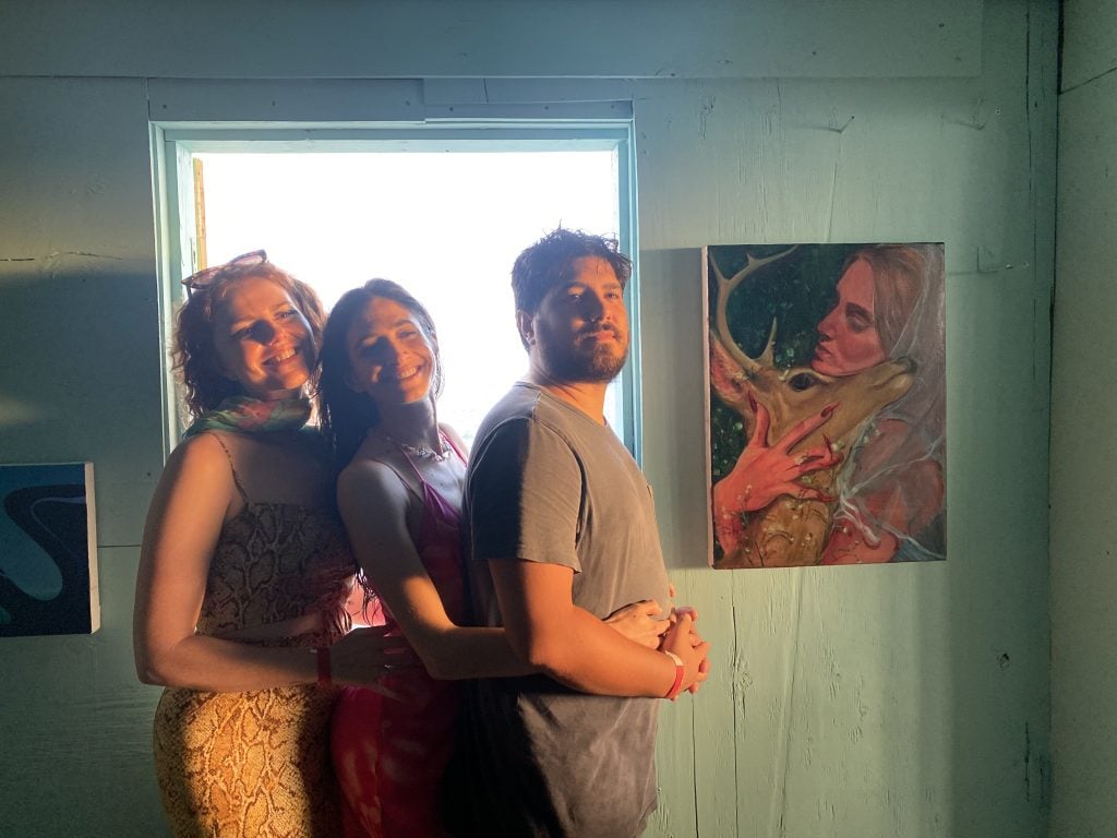 Samantha Joy Groff with Meredith Williams and Ricky Morales with Groff's painting The Hunter's Wife (2022) at Half Gallery's Stiltsville show. Photo by Sarah Cascone.