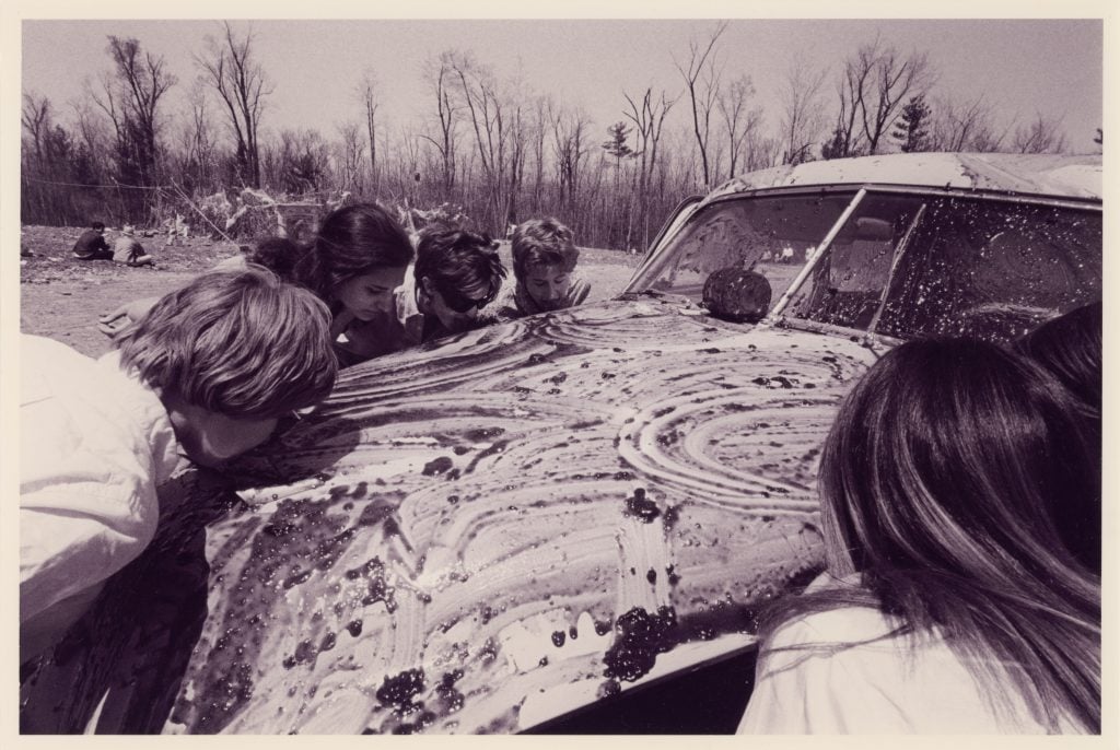 Female participants lick strawberry jam off of a wrecked car in Allan Kaprow's happening Household (1964). Photo: Cornell University Library.
