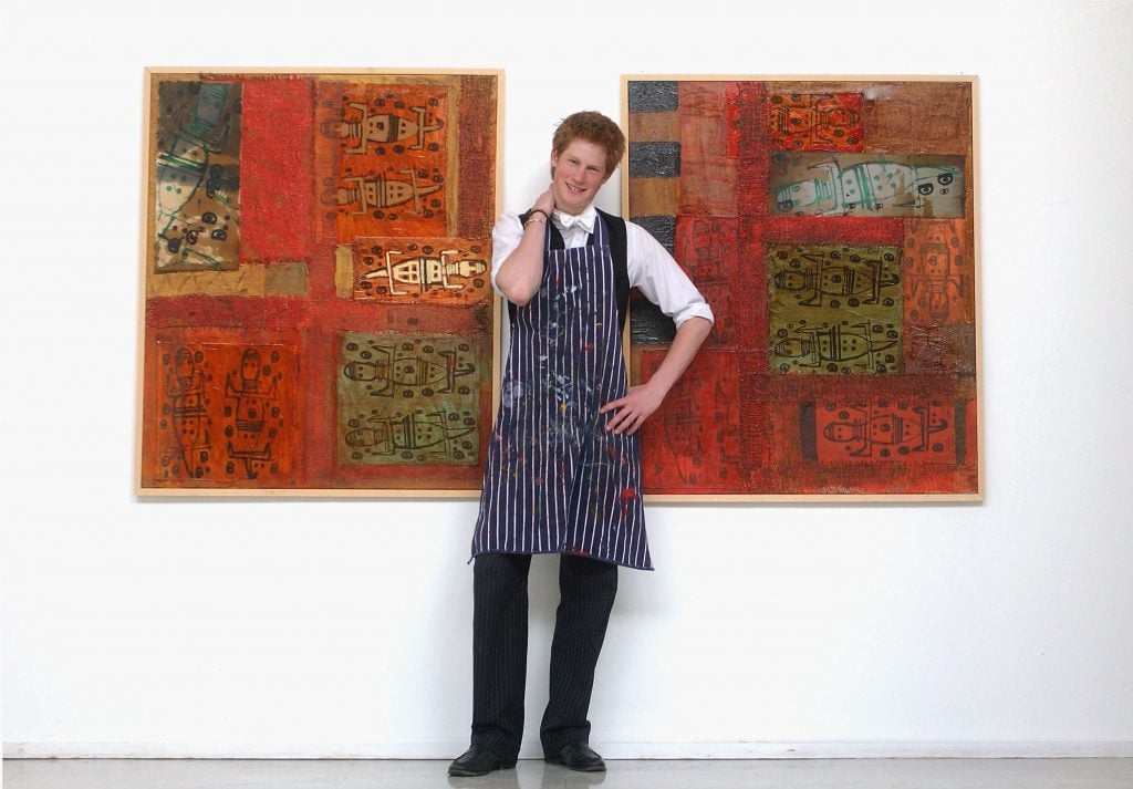 Prince Harry poses in front of two of his paintings in the drawing room at Eton College on May 12, 2003 in Windsor, England. The Royal Family on October 9, 2004, denied allegations that the prince had cheated in his art A-level. Sarah Forsyth, a former teacher of Harry at Eton, made the allegations as she prepared to take the college to an industrial tribunal claiming for unfair dismissal. Photo by Anwar Hussein/Getty Images.