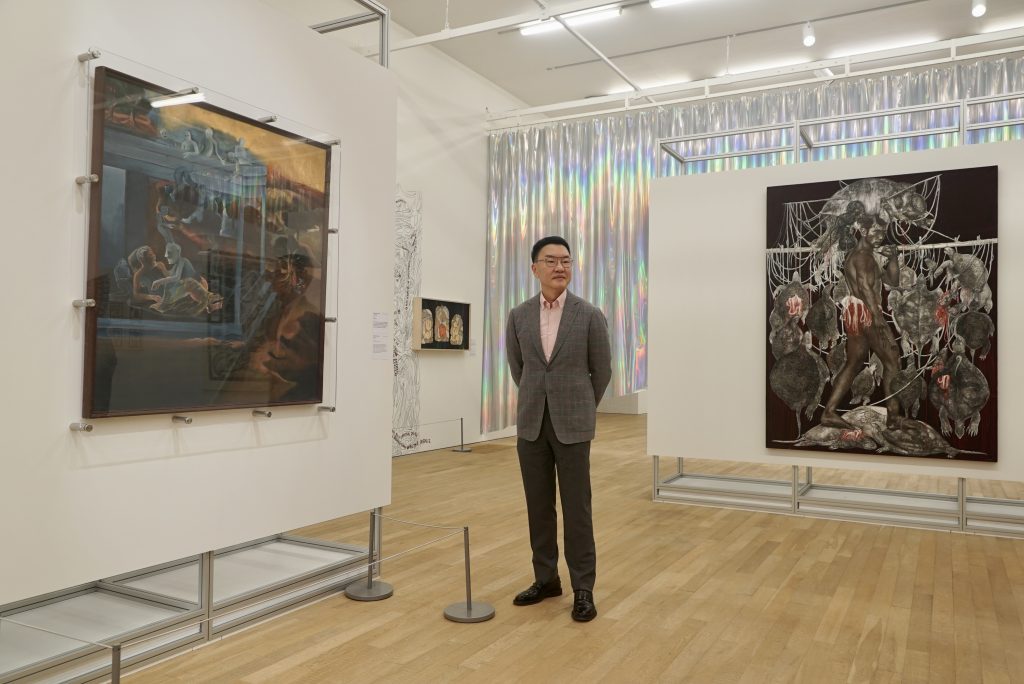 Hong Kong collector Patrick Sun and works from the collection of Sunpride Foundation on show at Myth Makers—Spectrosynthesis III at Tai Kwun Contemporary. From left to right: Bhupen Khakhar, <i>Visitors</i> (1998); Amy Lien & Enzo Camacho, <i>The Plot</i> (2021); Sornchai Phongsa, <i>Turtle's Spirits Totem 02</i> (2018). Courtesy of Sunpride Foundation.