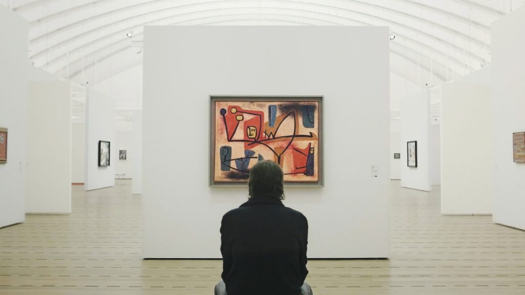 Still from the film Angel Applicant showing a person looking at an image of a Paul Klee work in a gallery.