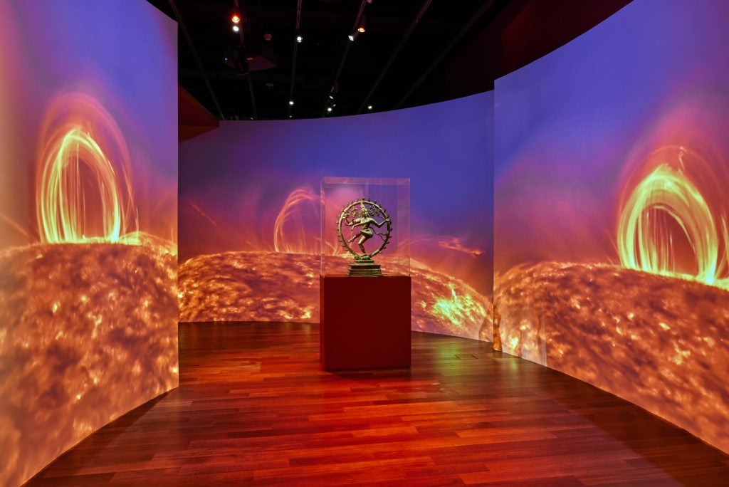 Installation view of "Beyond Bollywood: 2000 Years of Dance in Art" at the Asian Art Museum, San Francisco, with a statue of Shiva displayed against a backdrop of NASA footage of solar flares. Photo courtesy of the Asian Art Museum, San Francisco.