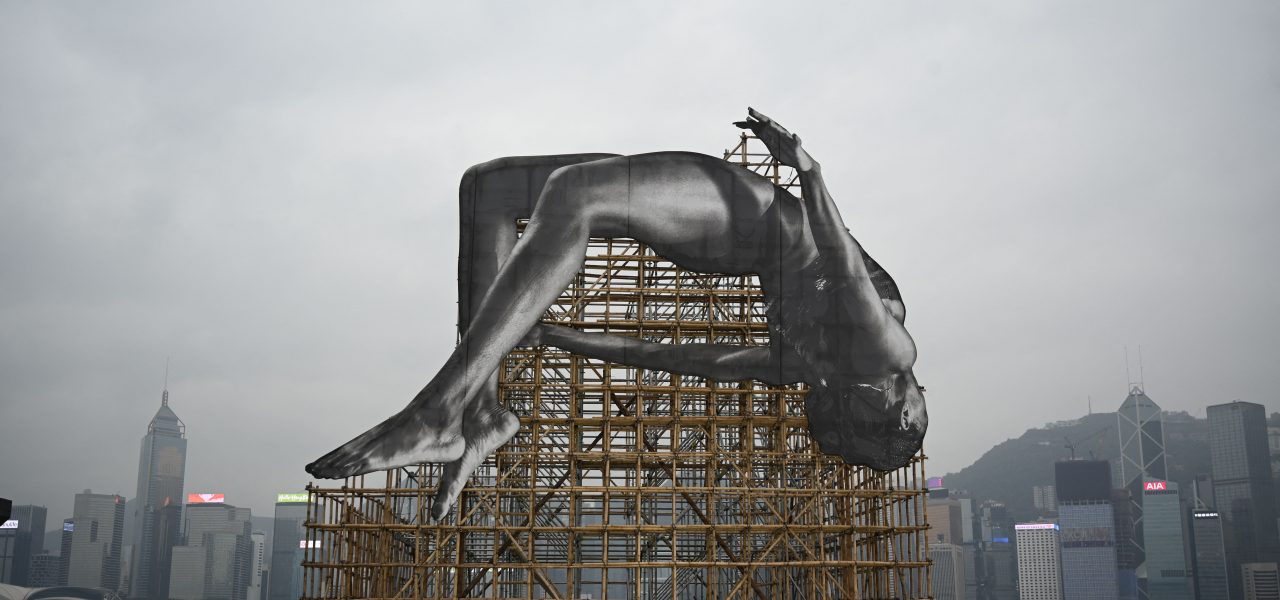 An installation by renowned French artist JR titled "GIANTS: Rising Up" is seen at a media preview in Hong Kong on March 13, 2023, depicting a larger-than-life high jumper adjacent to Hong Kong's Victoria Harbour. Photo by PETER PARKS/AFP via Getty Images.