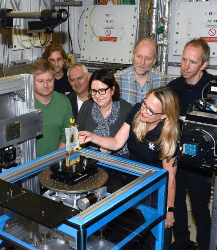 Francoise Berard (center), director of the library at the Institute de France, and the research group in the scanning room of the Diamond Light Source particle accelerator. Photo courtesy of the Vesuvius Challenge.