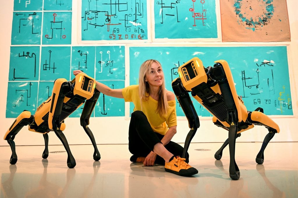 Agnieszka Pilat with her robot painting dogs, Basia Spot and Bunny Spot, at a press event announcing the National Gallery of Victoria Triennial 2023. Photo: William West / AFP via Getty Images.