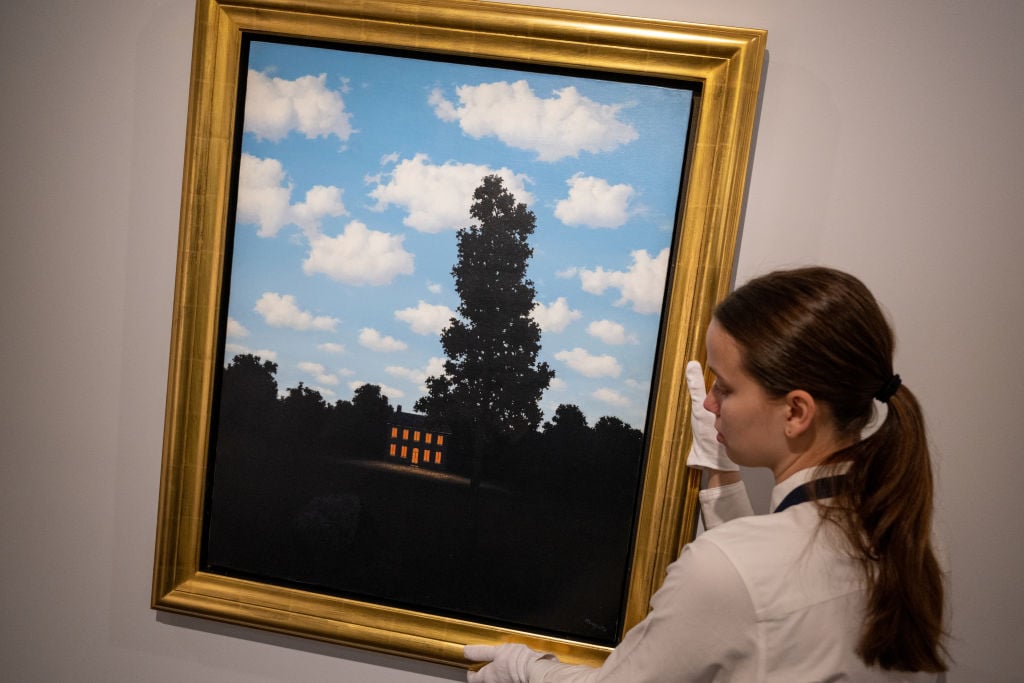 An art handler holds René Magritte's L’Empire des lumières, while on display during a press preview at Sotheby's on May 08, 2023 in New York City. Photo by Alexi Rosenfeld/Getty Images.