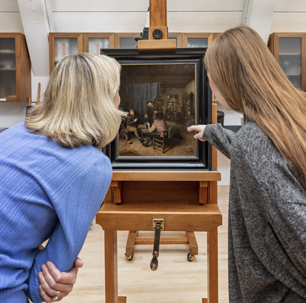 Victoria Reed, senior curator for provenance, and Christine Evers, curatorial research associate for provenance, examine Adriaen van Ostade's Customers Conversing in a Tavern (1671). Collection of the Museum of Fine Arts, Boston, promised gift of Susan and Matthew Weatherbie, in support of the Center for Netherlandish Art. Photo courtesy of the Museum of Fine Arts, Boston.