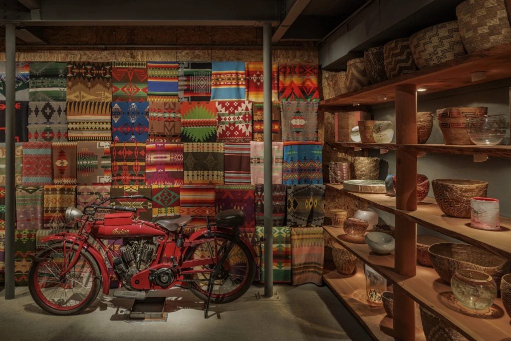 Pendleton blankets, a 1914 Indian Motorcycle, Native American baskets, and Dale Chihuly glass forms they inspired in the Northwest Room at the Boathouse, the artist's Seattle studio. Photo by Nathaniel Willson, ©2023 Chihuly Studio.