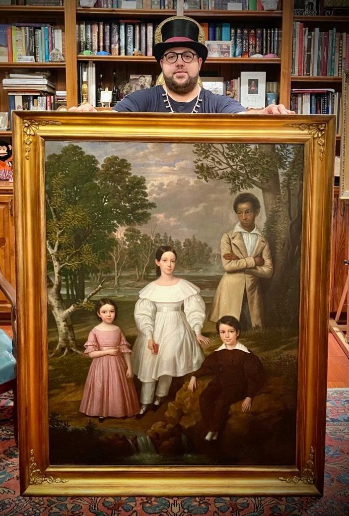 Jeremy K. Simien with <em>Bélizaire and the Frey Children</em>, attributed to Jacques Guillaume Lucein Amans, after it was restored, removing overpainting that obscured the figure of an enslaved boy. Photo courtesy of Jeremy K. Simien.” width=”693″ height=”1024″  ></p>
<p id=