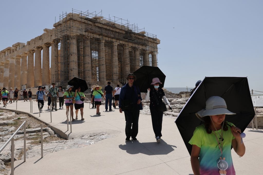 People use umbrella to protect themselves from the sun as they visit the Parthenon temple atop the Acropolis hill, during a hot weather in Athens, Greece on July 23, 2023. Visits to certain tourist sites, including the Acropolis, home to the Parthenon temple, in Athens, temporarily closed due to a fierce heatwave. Photo by Costas Baltas/Anadolu Agency via Getty Images.
