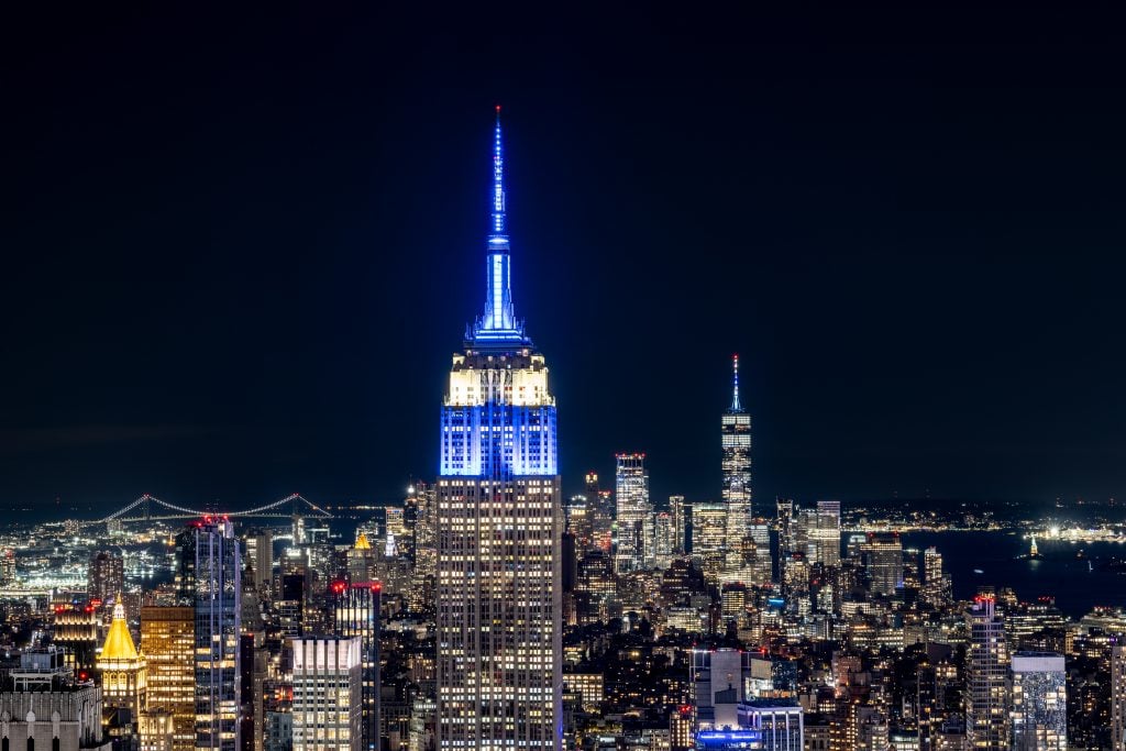 The Empire State Building is lit in blue and white in solidarity with Israel, with the Verrazzano Narrows Bridge on the left and the One World Trade Center on the right on October 07, 2023 in New York City. Photo by Roy Rochlin/Getty Images.