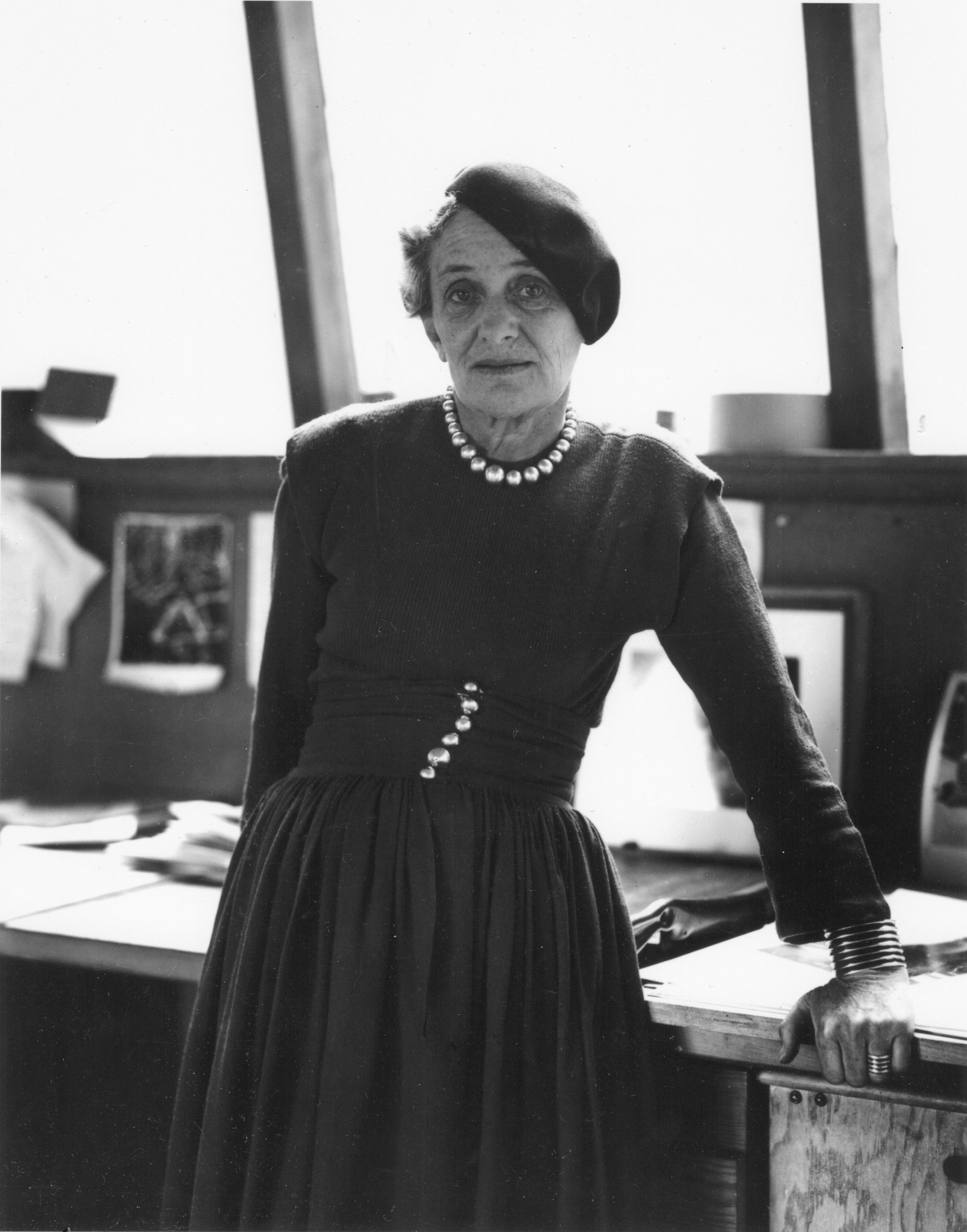 Photographer Dorothea Lange posing in a beret beside a desk