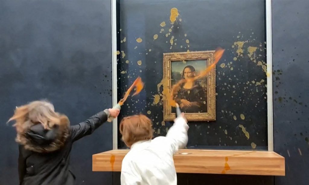 Two environmental activists from the collective "Riposte Alimentaire" throw orange soup at Leonardo Da Vinci's "Mona Lisa" at the Louvre museum in Paris, on January 28, 2024. The liquid is splattered all over the glass and wall.