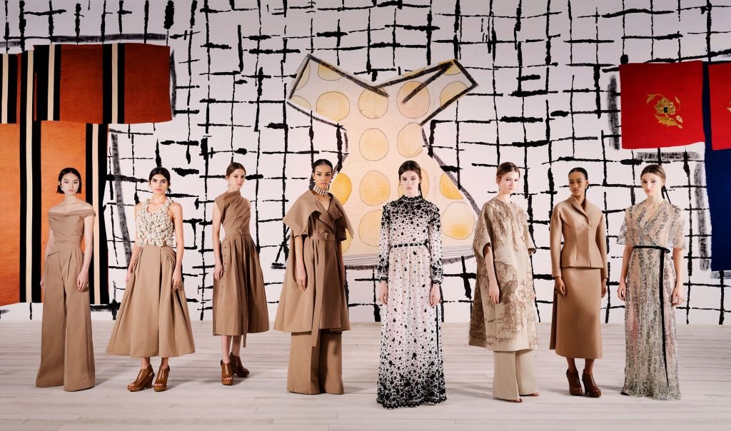 Models in designer Maria Grazia Chiuri's spring 2024 couture show with works by Isabella Ducrot in the background.