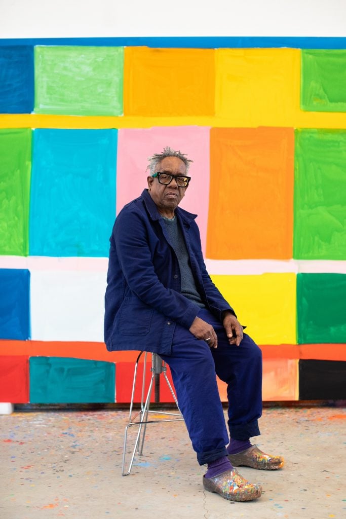 Portrait of Stanley Whitney sitting in front of a colorful painting.