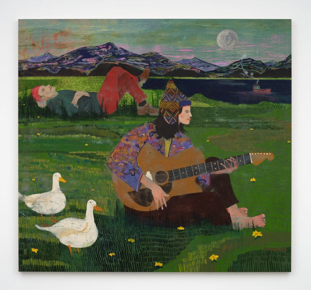 An outdoor scene features a young person playing a guitar, while behind him another person lays on his back staring into the sky. In the foreground, two white ducks stand on the green grass. 