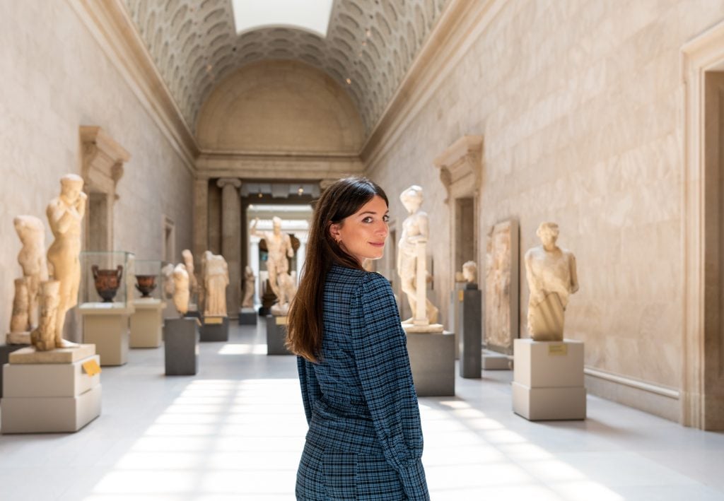Curator and author Katy Hessel standing in a hall full of ancient statues.