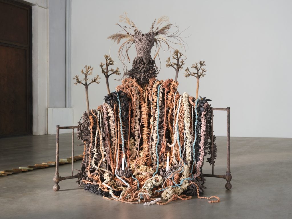 An art sculpture that consists of plants, earth, and natural ceramics draped on a structure to appear like a figure