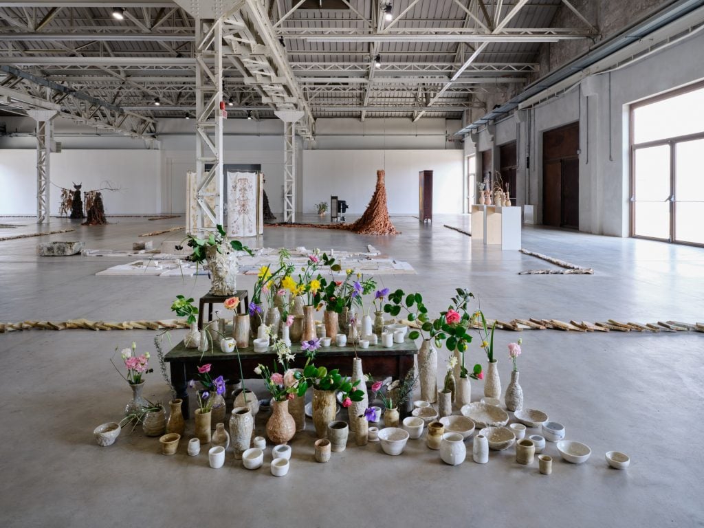 View of an art installation that consists of vases and flowers in a large industrial space