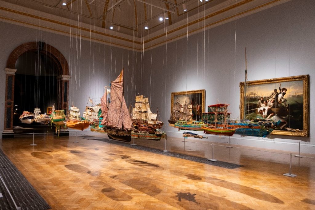 a fleet of little model boats suspended in a large gallery space