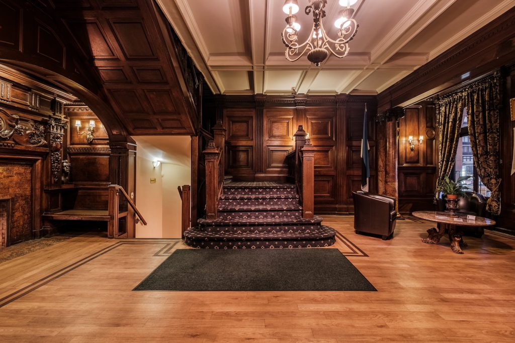 In a color photo, a wood-paneled lobby is seen head-on. Stairs are in the distance, and the ceiling is white.