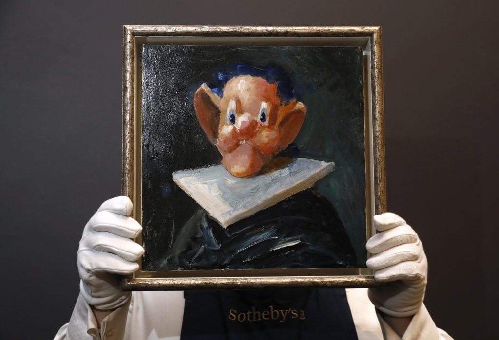 An auction house employee holds a painting in front of his face, depicting a character wiht oversized ears and cartoon eyes.
