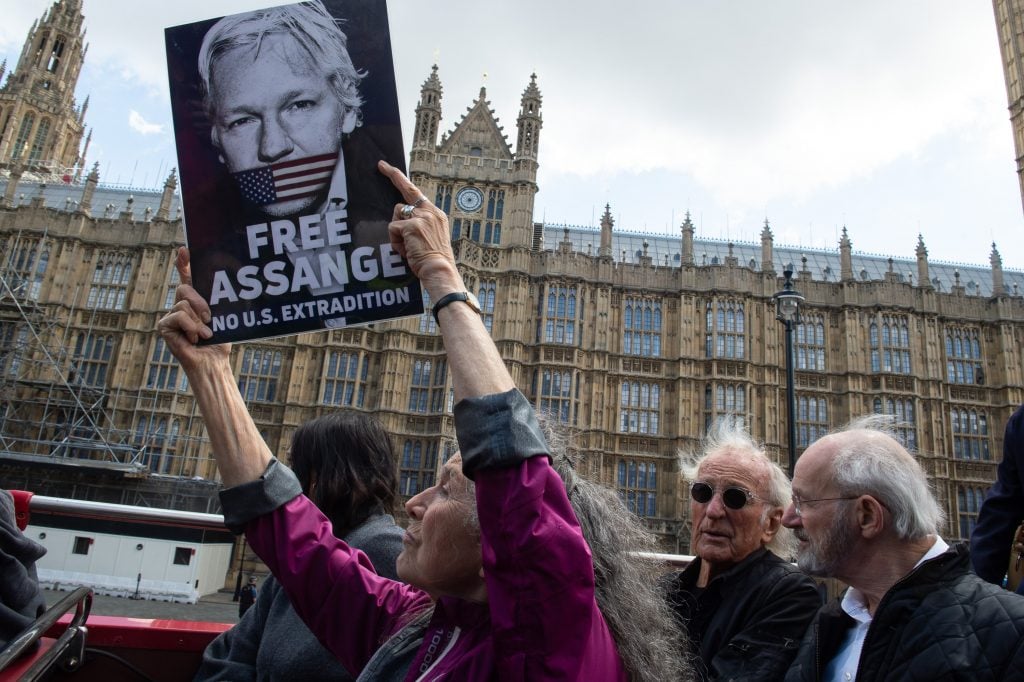 photograph of older woman holding free assange poster