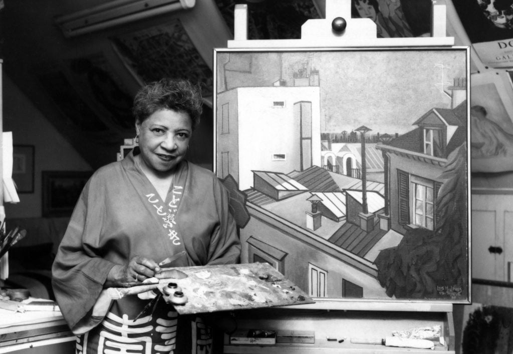 Lois Mailou Jones poses for a photograph near a painting. Jackson State University via Getty Images.