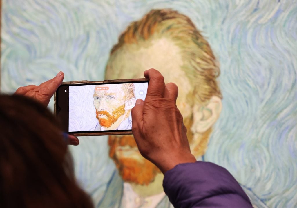 The image is of a woman holding a cell phone photographing van goghs 