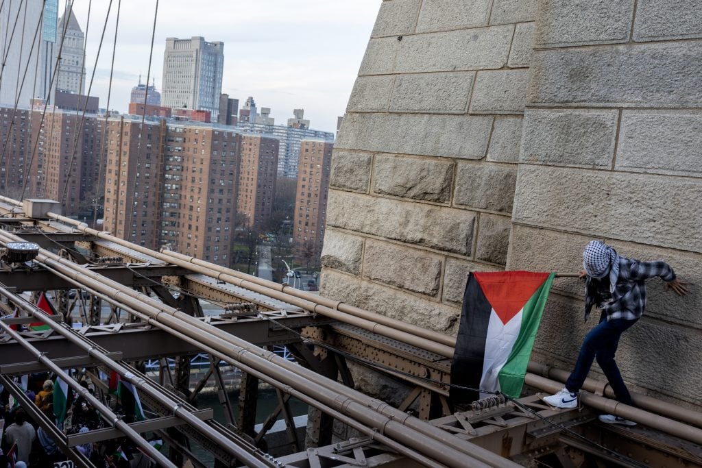 photograph of protester ontop of the bridge scaffolding with palestininian flag