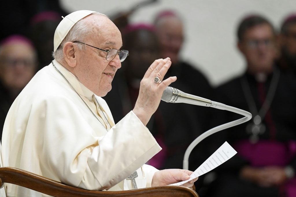 Profile photograph of Pope Francis raising his left hand at the podium