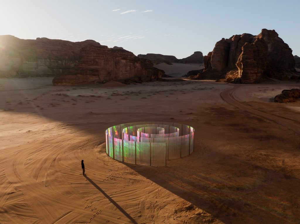 Photograph of glass walls set in a spiral reflecting iridescent light in a desert setting