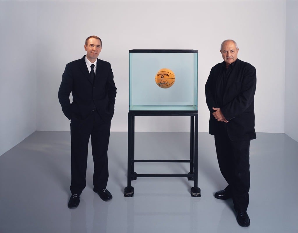 A color photograph of artist Jeff Koons and collector Dakis Joannou with Koons's sculpture One Ball Total Equilibrium Tank (Spalding Dr. JK 241 Series)