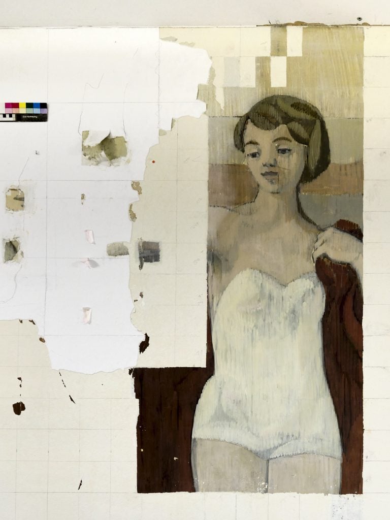This image shows a wall undergoing the process of removing a covering of white paint to reveal a mural by Gerhard Richter. The mural appears to be in a state of partial exposure, with various areas still obscured by remnants of the covering. The visible portion of the mural displays female figure in a mid-20th Century white bathing suit and short hair at the beach. The painting uses a limited color palette, with muted tones. The facial expression of the woman is neutral, with a slight tilt of the head. The condition of the mural suggests it has been hidden for a considerable time, indicated by the flaking and tearing of the layers on top. The presence of a color scale in the top left corner of the image indicates that this photograph is being used for documentation purposes, during the restoration process.