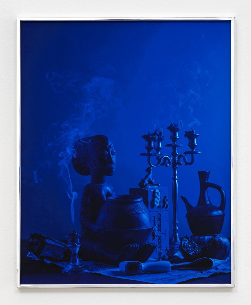 still life photograph bathed in deep blue of a candelabra along with some african artifacts and a pomegranite