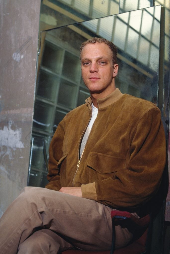 color photograph of photographer david seidner sitting with his legs crossed wearing a brown suede jacket