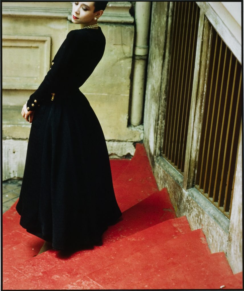 photograph of model tina chow in a black chanel dress with red lips, pearl necklace and earrings on a red staircase