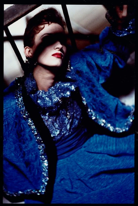 David Seidner photograph of model violetta sanchez in a cobalt blue ysl dress and coat sitting in a stairwell with vibrant red lips and the shadow of the railing masking her eyes