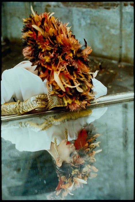 photograph of a woman in a autumn colored feather hat looking at herself on a mirrored table