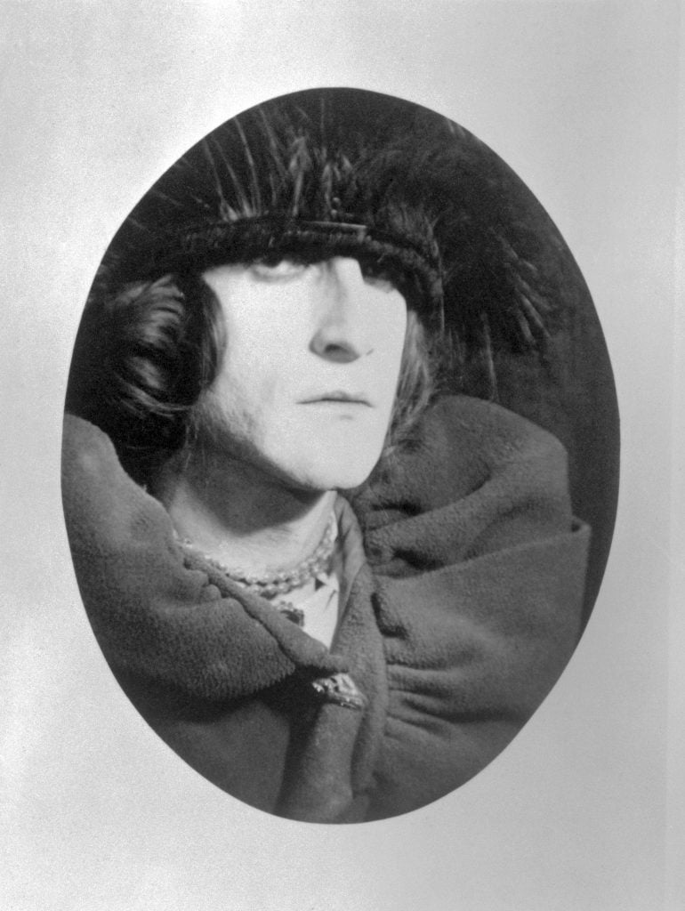 A photograph of artist Marcel Duchamp in a feathered hat and luxurious cape.