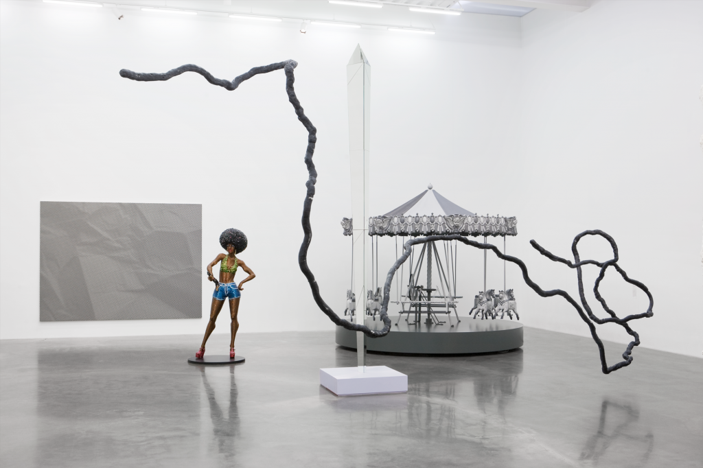 photograph of an installation view featuring scultptures of a silver caroulsel, woman with an afro and a large noodle like gray structure