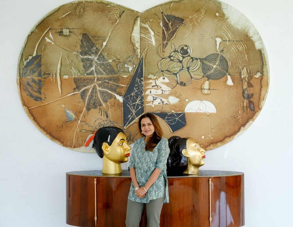 Sangita Jindal with two gilded heads by Ravinder Reddy and Jitish Kallat’s Echo Verse (2022) on the wall.