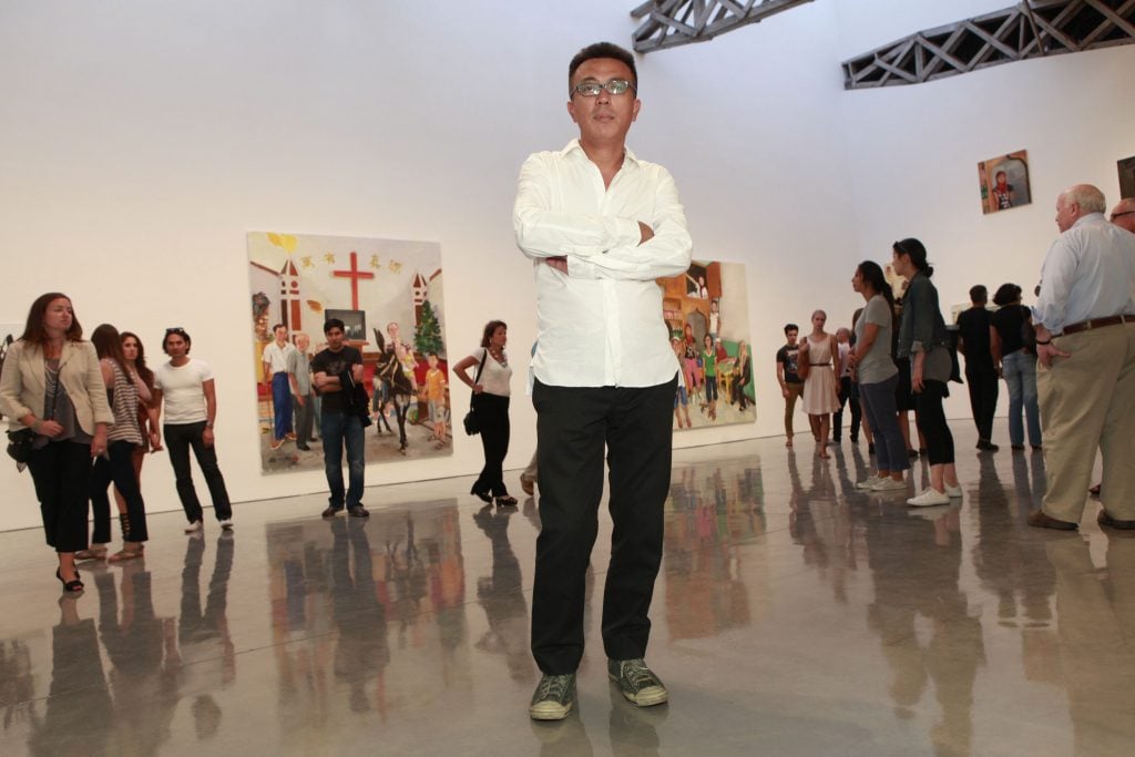 艺术家刘晓东身穿白色纽扣，双臂交叉站在玛丽·布恩画廊内